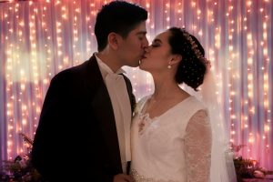 man in black suit kissing woman in white floral lace wedding dress